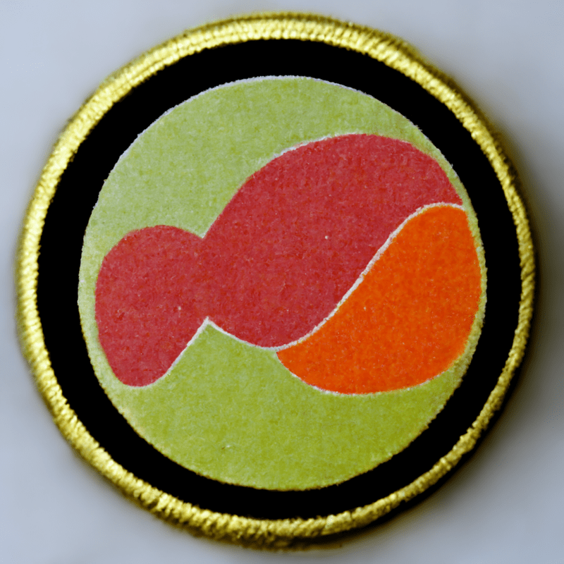 Round patch-style badge (black/yellow with orange shapes)