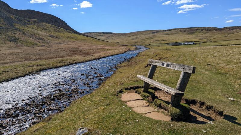 Bench next to the River Tees. Hills and blue sky in background