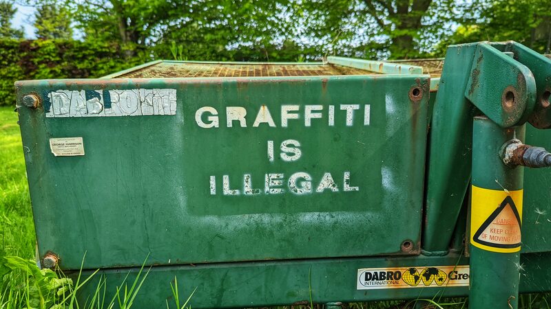 Graffiti stencil on the side of grass cutting equipment: GRAFFITI IS ILLEGAL