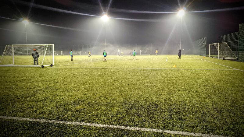 Photo of older teenagers in a football training session under floodlights on an artificial grass surface.