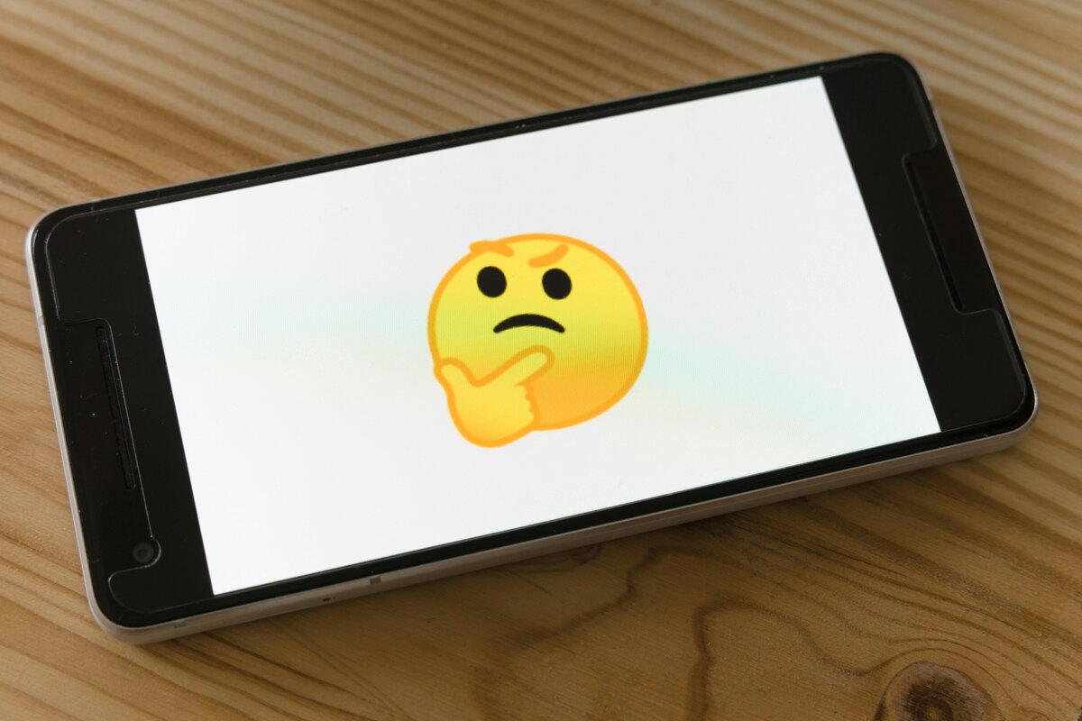 Smartphone displaying a thinking face emoji on a wooden surface.