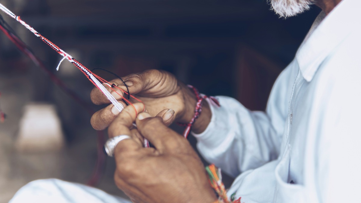 Close-up photo of someone braiding together different coloured strands with their hands.