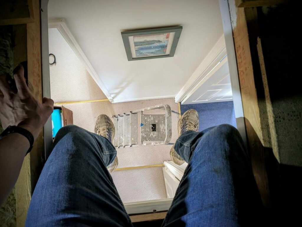 Looking down at my legs and feet hanging down from the loft hatch. The ladder is visible below.